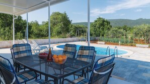 A covered outdoor seating area with a pool, chairs, and a table with fruit and a bottle. - Gorgeous home in Lozovac (Lozovac)