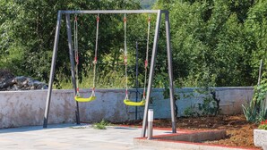 A swing set with two yellow swings, a concrete wall, and a pool in the foreground. - Gorgeous home in Lozovac (Lozovac)