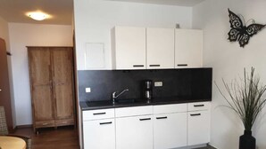 A compact kitchen with white cabinets, a black countertop, and a coffee maker. - (157) 1- room apartment - apartment complex Yachthafenresidenz (Kühlungsborn)