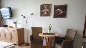 A cozy room with a bed, a small table with a vase, two wicker chairs, a cabinet, and a television on the wall. - (157) 1- room apartment - apartment complex Yachthafenresidenz (Kühlungsborn)