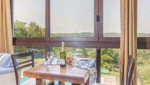 Ein Tisch mit einer Weinflasche und Gläsern, vor einer malerischen Aussicht durch große Fenster.
