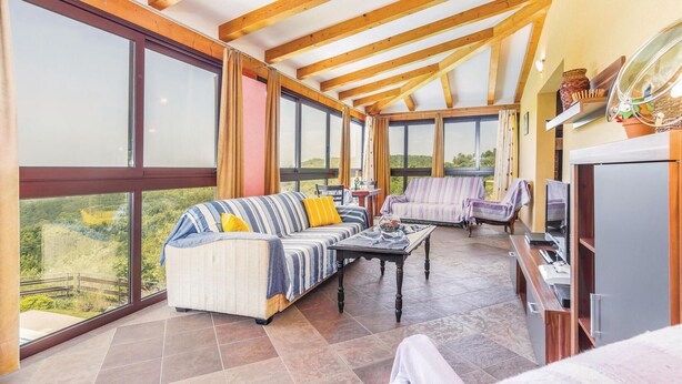 Ein geräumiger Wintergarten mit großen Fenstern, einer Couch, einem Sessel und einem Fernseher.