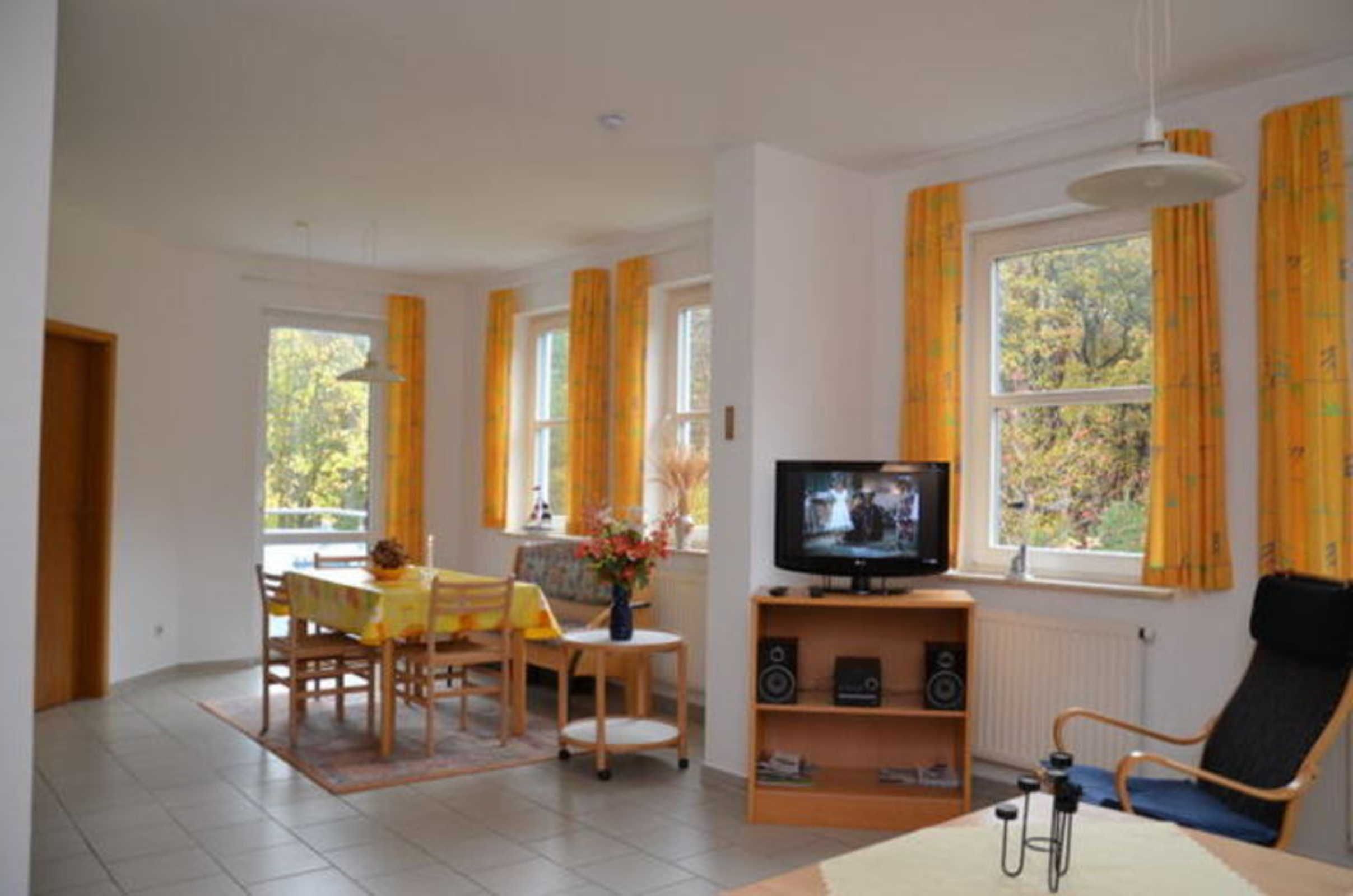Un salon avec une télévision, une table à manger avec des chaises, un canapé et une fenêtre avec des rideaux.