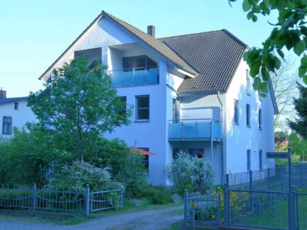 A two-story house with a balcony, a fenced yard, and a clear sky.