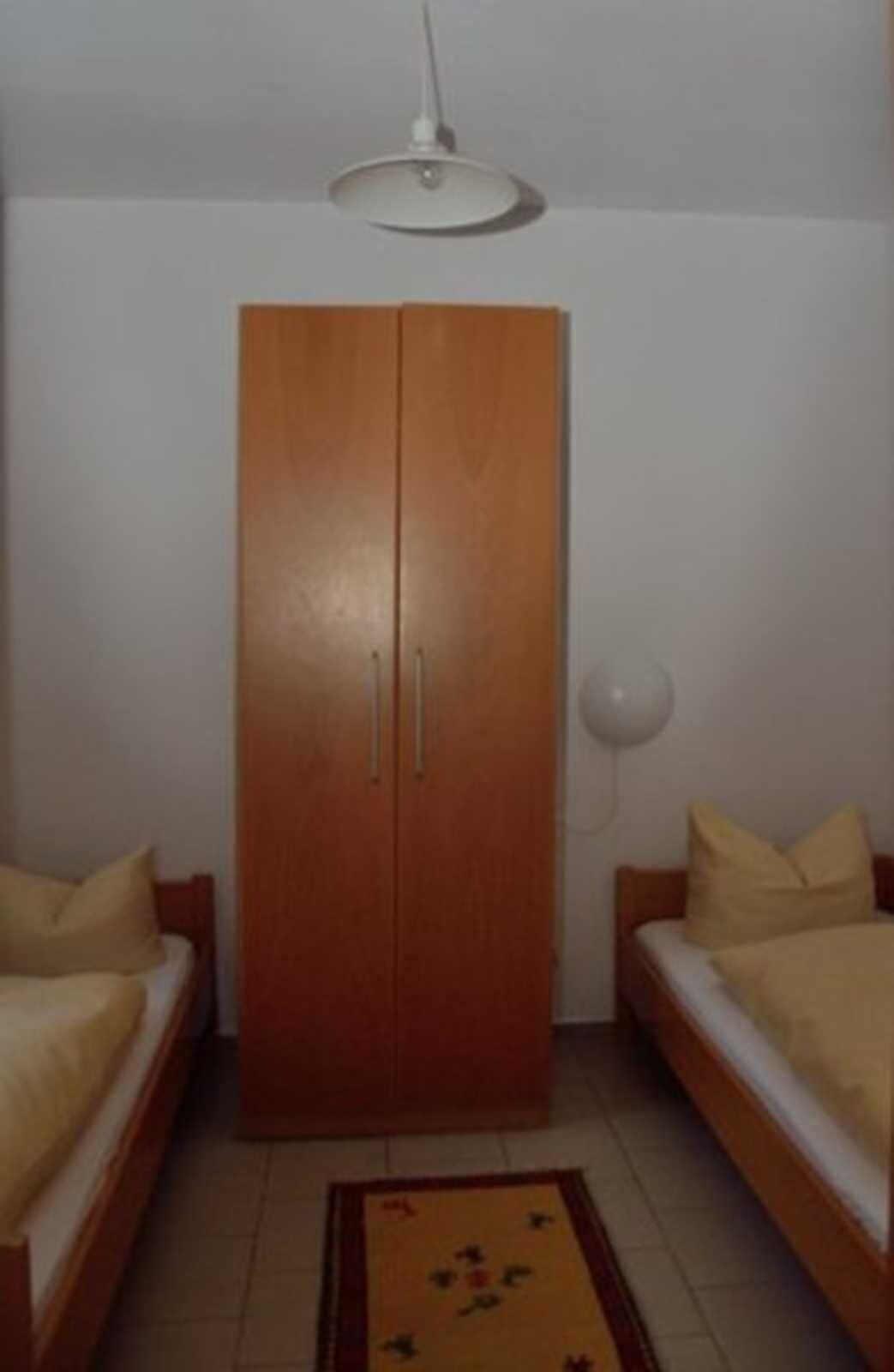 Ein Zimmer mit Schrank, zwei Betten, Deckenleuchte und Stehlampe.