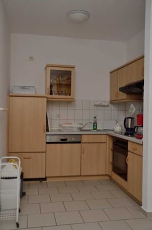 A small kitchen with wooden cabinets, a tiled backsplash, a dishwasher, a kettle, and a coffee maker.