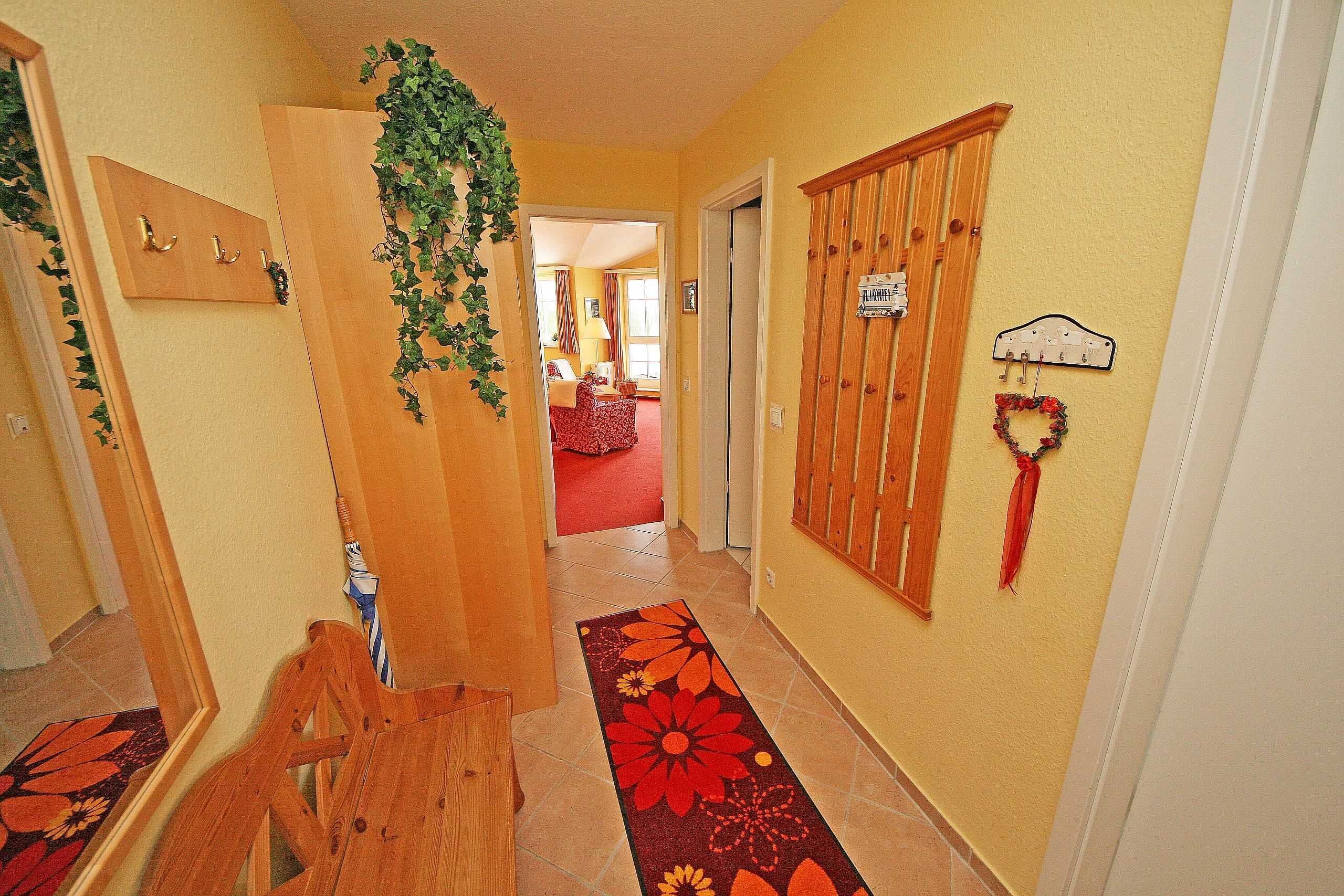 Un corridoio con una panca in legno, un tappeto floreale e una porta che dà su una stanza con un tappeto rosso.