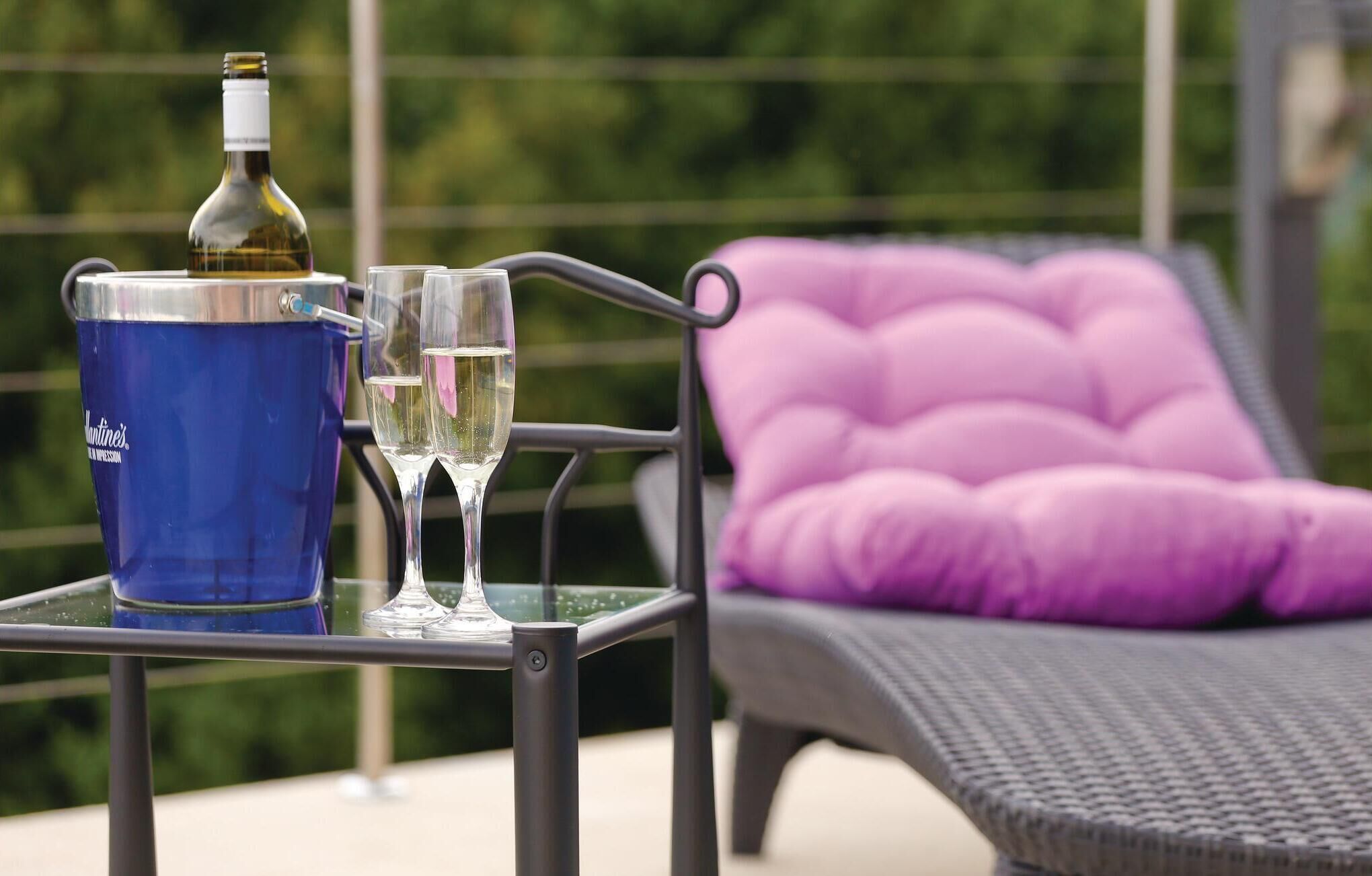 Ein Tisch mit einer Flasche und Gläsern, ein blauer Eimer und ein violett gepolsterter Stuhl.