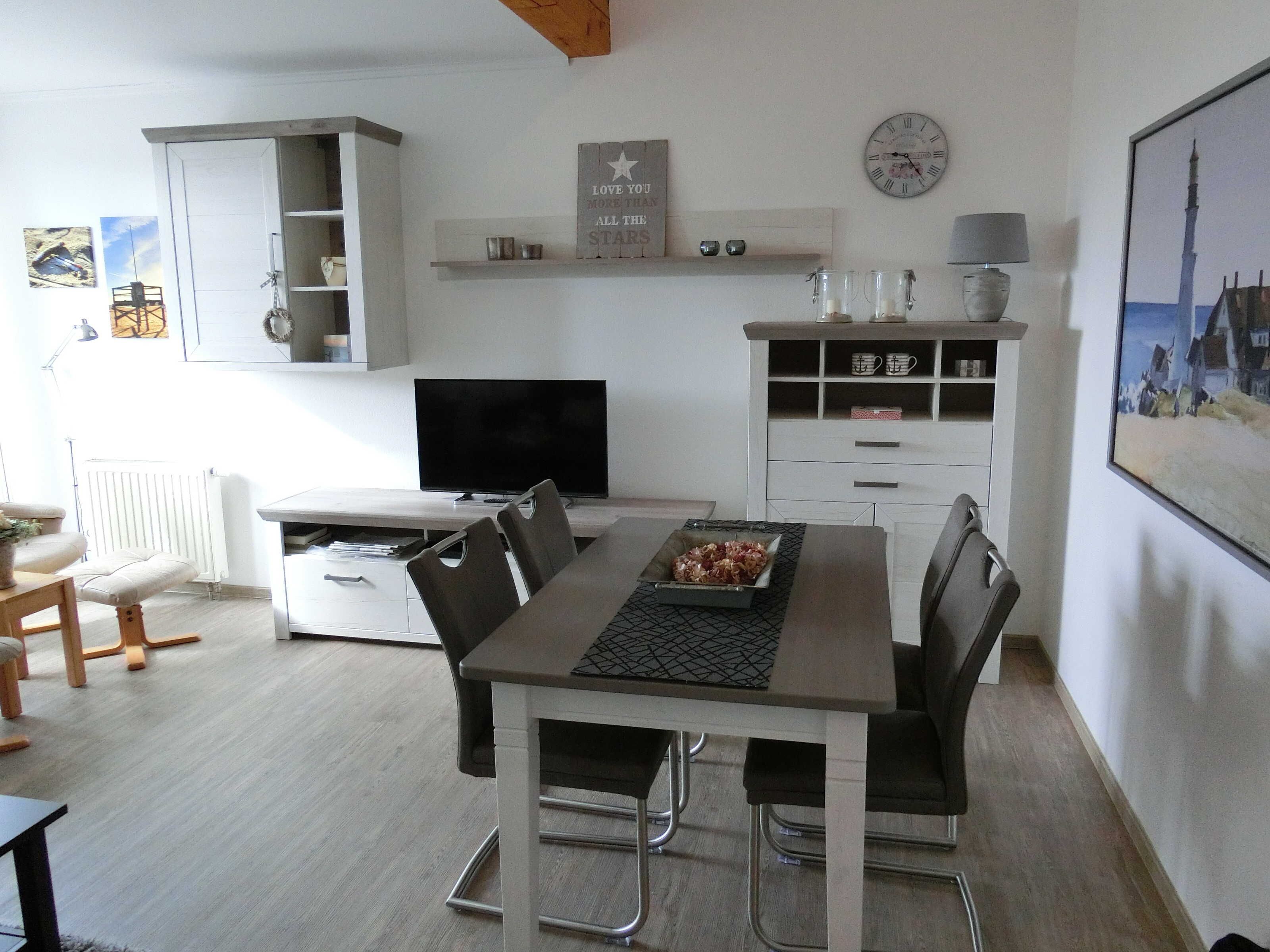 Una cocina moderna con comedor, armarios blancos, un televisor de pantalla plana y un reloj en la pared.