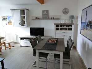 A modern kitchen with a dining area, white cabinetry, a flat-screen TV, and a clock on the wall.