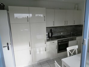 Una cocina moderna con armarios blancos, un lavamanos de acero inoxidable y un horno empotrado.