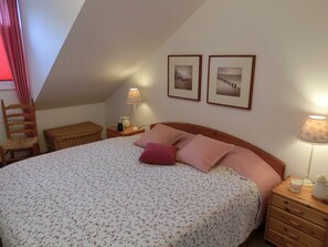 A bedroom with a bed, two framed pictures on the wall, a nightstand with a lamp, a chair, and a small table. - Apartment 52 Residence Bellevue Usedom DSL-WLAN free of charge - Apartment 52 (Zinnowitz)