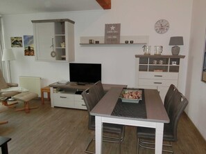 A living room with a TV, a dining table with chairs, a sofa, a cabinet, and a clock on the wall.