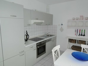 A kitchen with white cabinets, a stove, oven, sink, and a dining area with a white table and blue bowl.