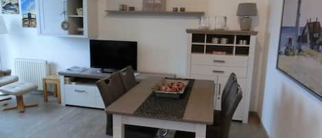 A modern living room with a dining table, chairs, a TV, a fireplace, shelves, and a clock.