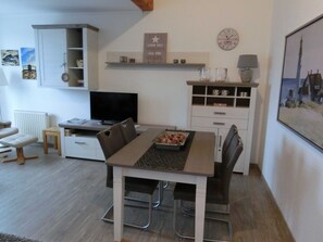 Una sala de estar moderna con una mesa de comedor, sillas, televisor, chimenea, estanterías y un reloj.