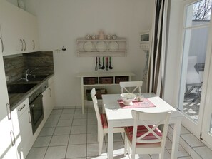 A kitchen with a sink, stove, and white cabinets. There is a dining table with chairs and a window with curtains. - Apartment 52 Residence Bellevue Usedom DSL-WLAN free of charge - Apartment 52 (Zinnowitz)