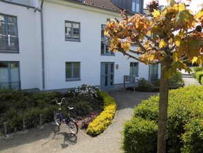 A building with a paved entrance, a bicycle parked outside, and a well-maintained garden with various plants.