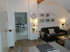 A living room with a black sofa, a coffee table, a small side table with a lamp, and a dining area with a white table and chairs. - Apartment 52 Residence Bellevue Usedom DSL-WLAN free of charge - Apartment 52 (Zinnowitz)