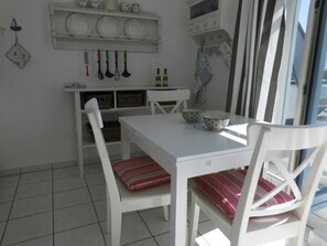A white dining table with two chairs, a white cabinet with dishes, and kitchen utensils hanging on the wall.