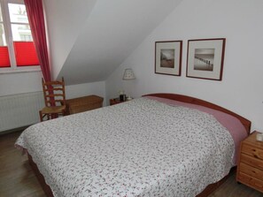 A bedroom with a bed, a chair, a nightstand, and two framed pictures on the wall.