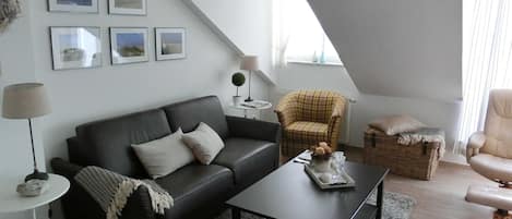 A modern loft-style living room with a black leather sofa, a coffee table, a plaid armchair, and a wicker basket.