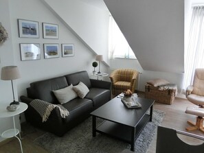 A modern loft-style living room with a black leather sofa, a coffee table, a plaid armchair, and a wicker basket.