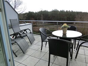 A balcony with a table and chairs, a potted plant, and a view of trees.
