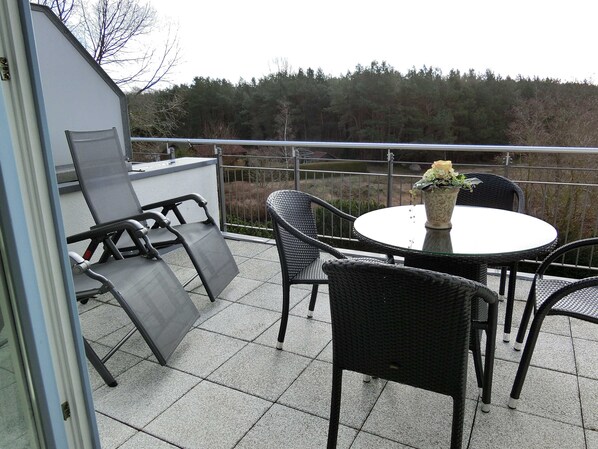 A balcony with a table and chairs, a potted plant, and a view of trees.