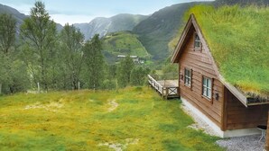 Eine Holzhütte mit Grasdach, eingebettet in eine gebirgige Landschaft mit Bäumen.
