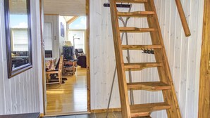 Ein Zimmer mit einer Holzleiter, die an einer Wand lehnt, einer Tür zu einem anderen Raum und einem Fenster mit Jalousien.