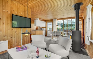 A cozy cabin interior with a TV, seating area, and a wood-burning stove. - 2 bedroom beach front home in Bindslev (Bindslev)