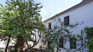 Edifício branco com várias janelas e área de jardim com diversas plantas e árvores.