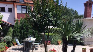Eine Terrasse mit Tisch und Stühlen, umgeben von Kübelpflanzen und einem kleinen Baum.
