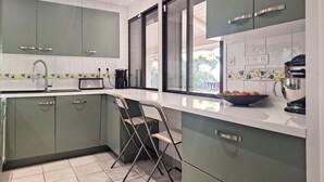 A modern kitchen with green cabinets, a white countertop, a sink, a toaster, a coffee maker, and a bowl of fruit. - Stunning home in Vias (Vias)