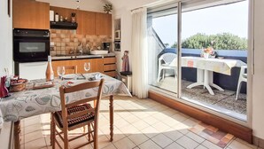 Una cocina con comedor, una mesa y sillas, vistas a través de un ventanal y un reloj en la pared.