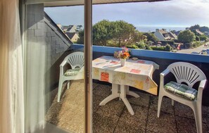 A balcony with a table and two chairs, a vase with flowers, and a view of houses and trees. - Beach front apartment in Clohars Carnoet (Clohars Carnoet)