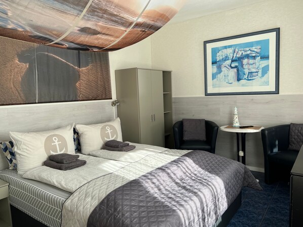Ein Hotelzimmer mit Bett, Schreibtisch, Stuhl, Kleiderschrank und einem Bild an der Wand.