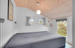 Un dormitorio con una cama grande, techo de madera y ventanas con cortinas.