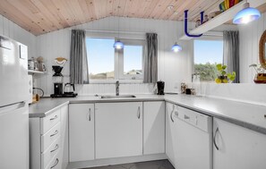 A modern kitchen with white cabinets, a built-in dishwasher, and a window with striped curtains. - 3 bedroom beautiful home in Hjørring (Hjørring)