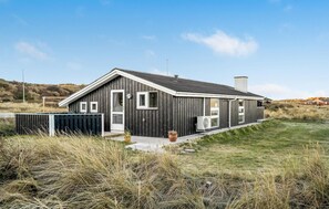Una casa moderna de madera con techo inclinado, un ventanal grande y un pequeño porche.