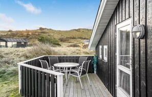 Una terraza de madera con una mesa, sillas, una ventana y una puerta.