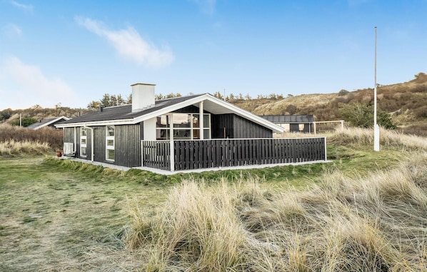 Una casa moderna con techo inclinado, ventanas grandes y una terraza de madera.