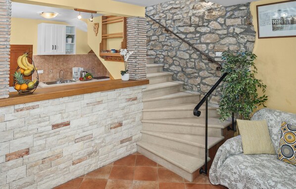Una cocina con pared de piedra, encimera de madera y una escalera que lleva a una sala de estar con sofá y planta.