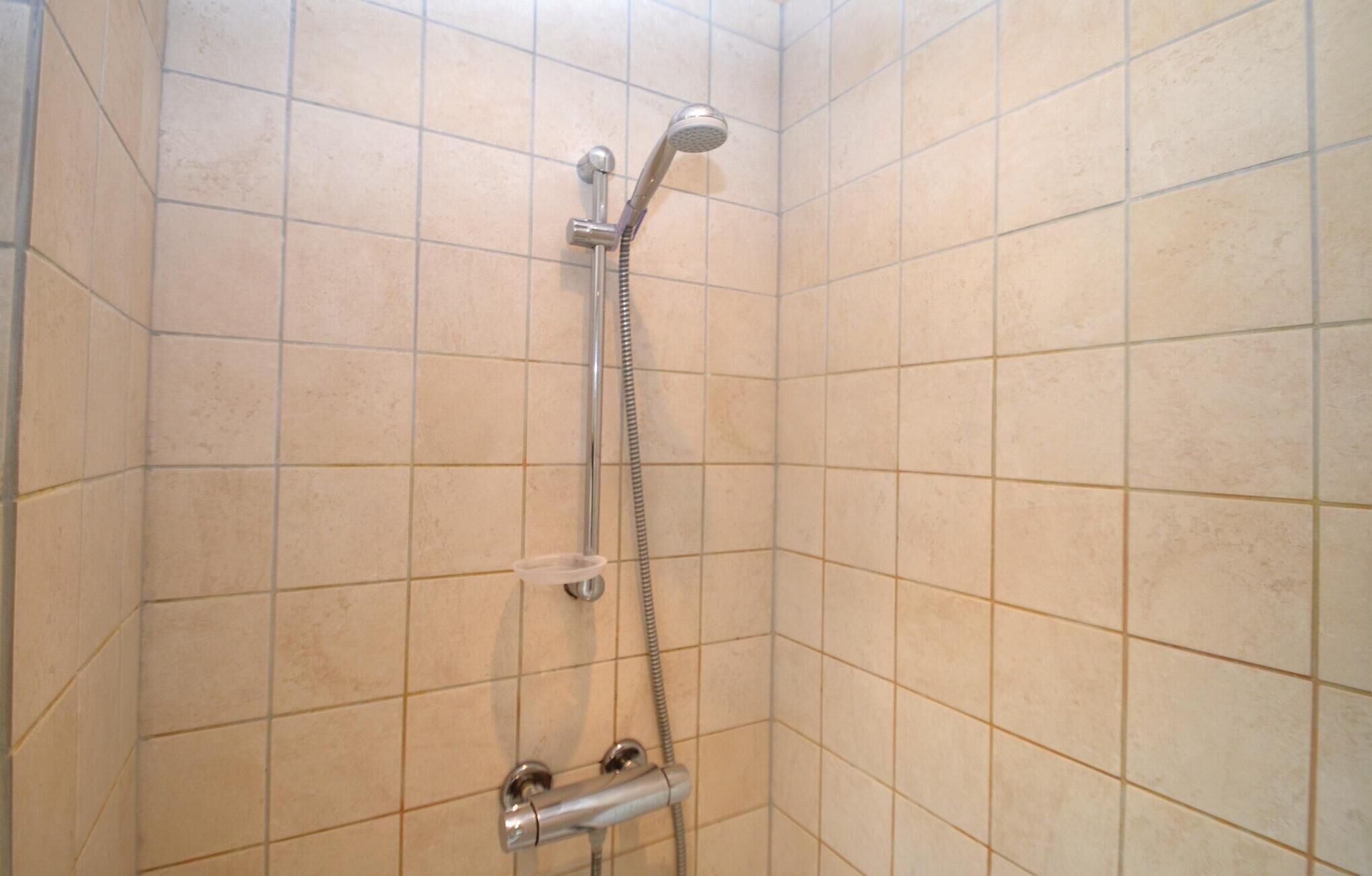 A shower with a handheld showerhead and a wall-mounted control valve.
