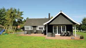 Ein Haus mit überdachter Terrasse, Schornstein und einem Spielbereich mit Rutsche.