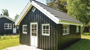Ein kleines, dunkelholziges Geb äude mit weißer Tür und Fenstern, einem geneigten Dach und einem gepflasterten Eingang.