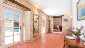 A spacious room with a stone wall, a wooden ceiling, and a tiled floor. There is a door leading to a balcony with a pool, and a table with a vase of flowers. - Pet friendly home in Kringa (Kringa)