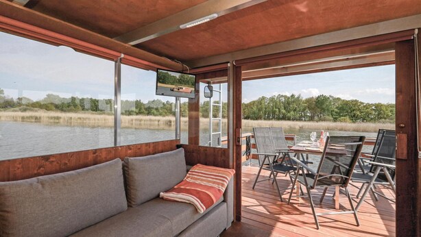 Une terrasse en bois avec un canapé et une table à manger, donnant sur une étendue d’eau et des arbres.