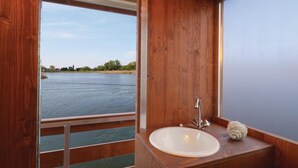 Une salle de bain avec un intérieur en bois, un lavabo blanc et une vue sur une rivière.